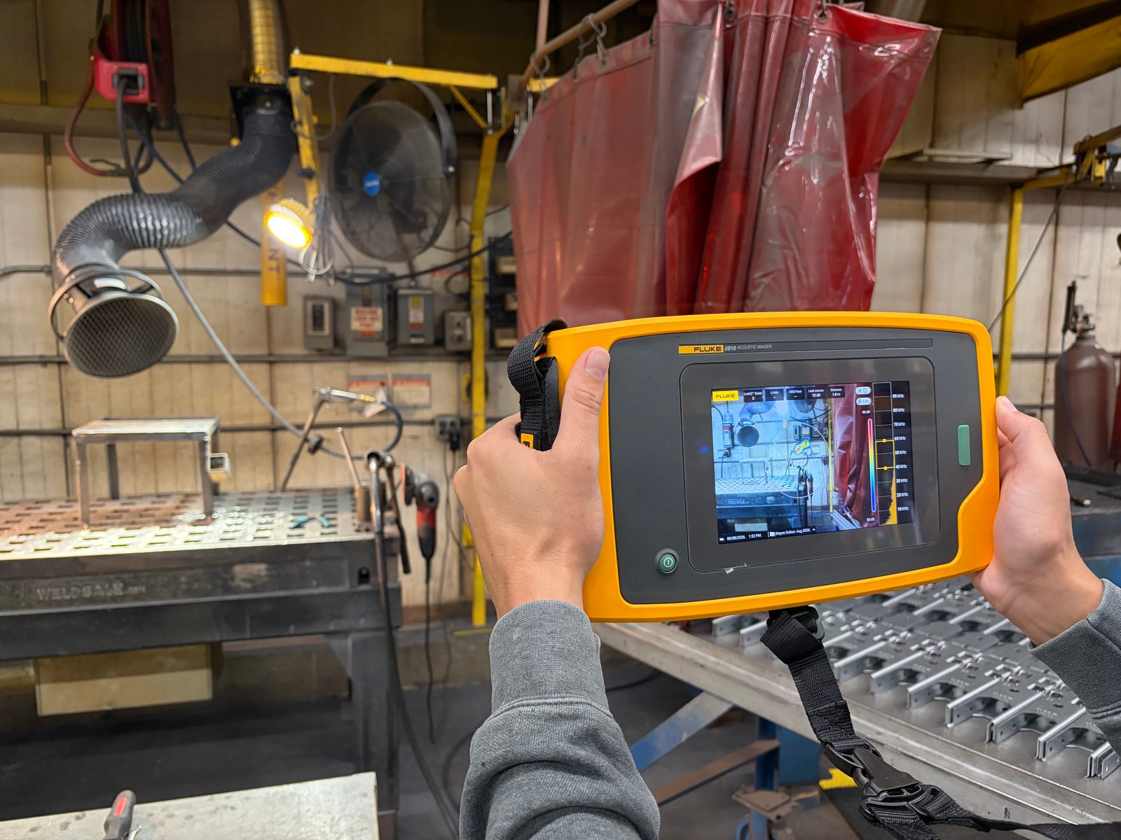 Technician using a Fluke acoustic imaging camera to visually locate a compressed air leak, with the SoundMap overlay pinpointing the leak source on the imager's display